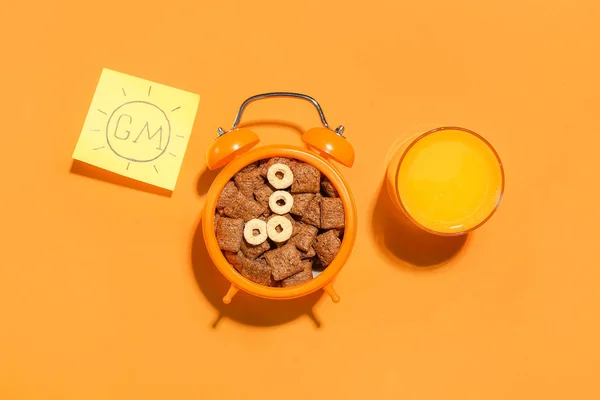 Alarm clock with corn pillows and glass of juice on color background