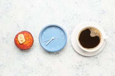 Çalar saat, lezzetli kek ve arka planda bir fincan kahve.