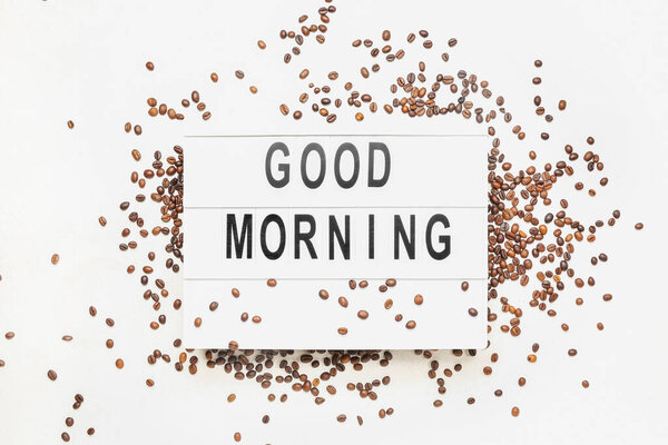 Board with text GOOD MORNING and coffee beans on light background