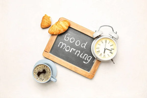 Chalkboard with text GOOD MORNING, alarm clock, cup of coffee and croissants on light background