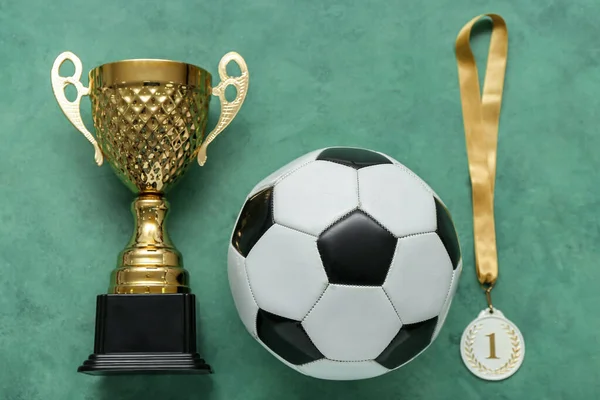 Gold cup with first place medal and soccer ball on green background