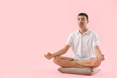 Young man meditating on pink background