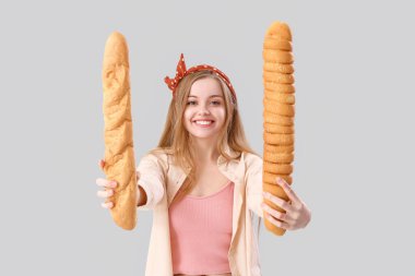 Young woman with fresh baguettes on grey background