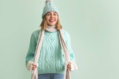 Frozen young woman in winter clothes on green background