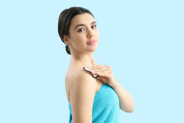 Mavi arka planda pamuklu ped ile makyajı kaldıran genç bir kadın.