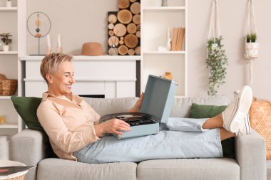 Evde kanepede pikap takmış olgun bir kadın.