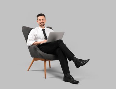 Gri arka planda dizüstü bilgisayarla çalışan yakışıklı iş adamı.