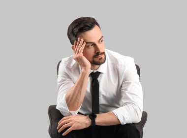 Gri arka planda koltukta oturan yakışıklı iş adamı