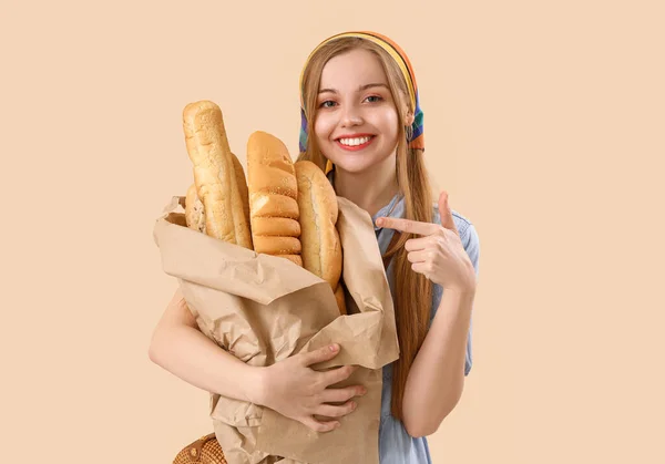 年轻女人指着米色背景的新鲜面包 — 图库照片