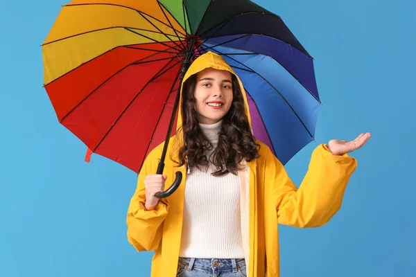 Teenage girl in raincoat with umbrella on blue background