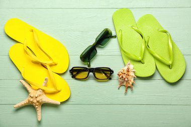 Güneş gözlüklü terlikler ve yeşil ahşap arka planda deniz kabuğu.