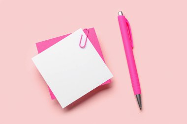 Pembe zemin üzerinde ataç ve kalem olan yapışkan notlar.