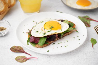 Yağda yumurta ve açık arkaplanda yeşillikler olan lezzetli bir sandviç.