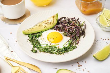 Lezzetli sahanda yumurta, avokado ve açık arkaplanda yeşillikler.