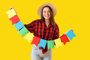 Sarı arka planda bayrakları olan genç bir kadın. Festa Junina (Haziran Festivali) kutlaması