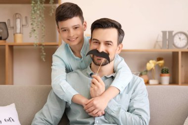 Evde kağıt bıyıklı babasının ve küçük oğlunun portresi.