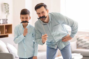 Evde kağıt bıyıklı babasının ve küçük oğlunun portresi.