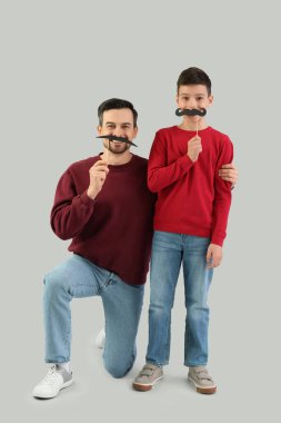 Açık arkaplanda kağıt bıyıklı babasının ve oğlunun portresi.