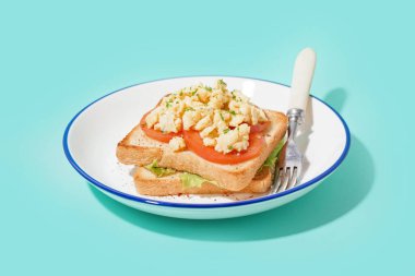 Mavi arka planda lezzetli çırpılmış yumurtalı sandviç tabağı.