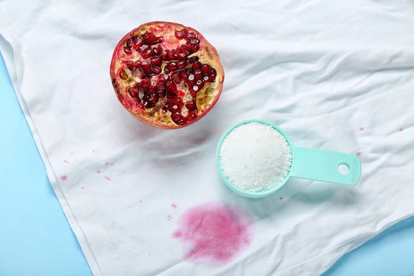 Laundry detergent with pomegranate and stained clothes on blue background, closeup