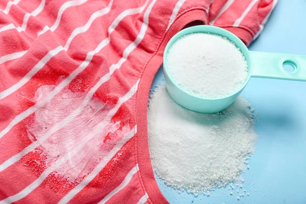 Laundry detergent with stained clothes on blue background, closeup
