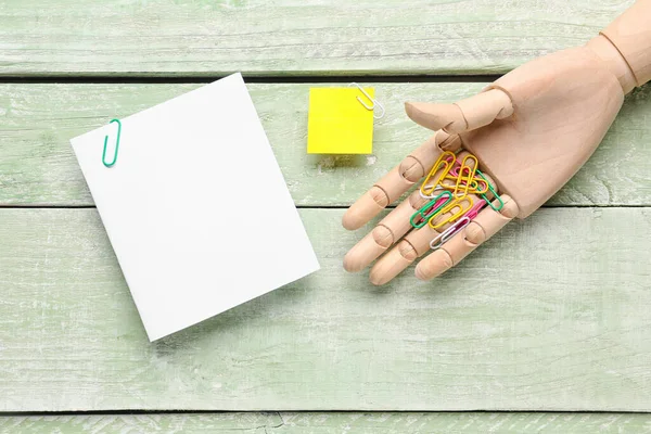 Sticky note and wooden hand with paper clip on green wooden background
