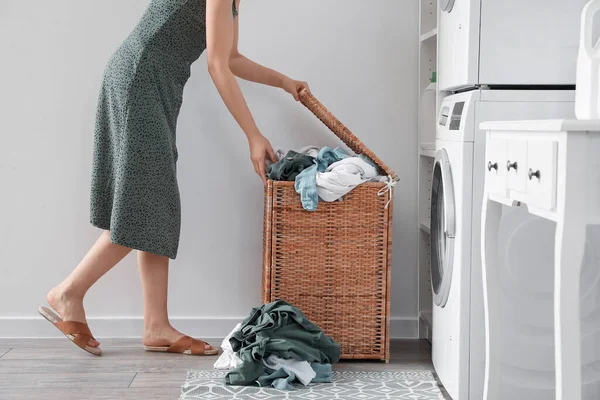 Woman with dirty clothes in laundry basket at home