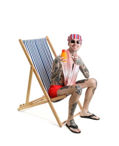 Tattooed man with sunscreen cream sitting on deck chair against white background