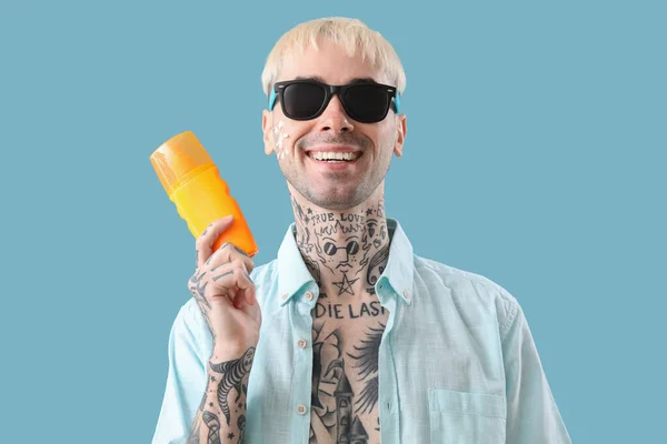 Tattooed man with sunscreen cream on light blue background