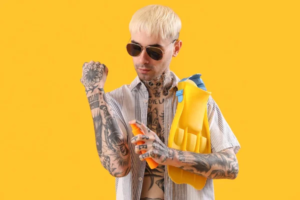 Tattooed man applying sunscreen cream on yellow background