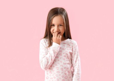 Little girl biting nails on pink background