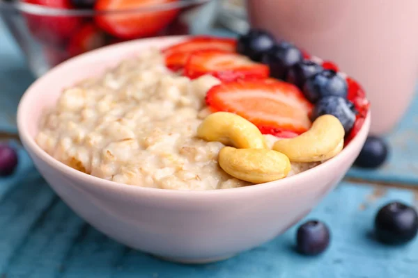 stock image Bowl with tasty oatmeal, strawberries, blueberries and cashew on blue wooden background