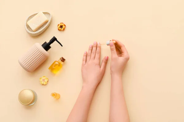 Female hands with cuticle oil and cosmetic products on color background