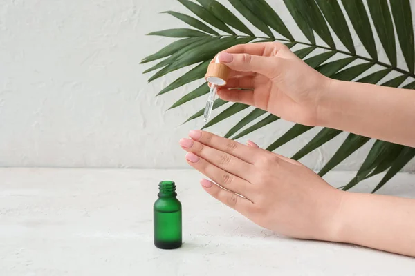Female hands with bottle of cuticle oil and palm leaf on light background