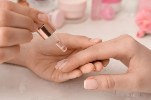Manicure master applying cuticle oil onto female fingernails on light background, closeup