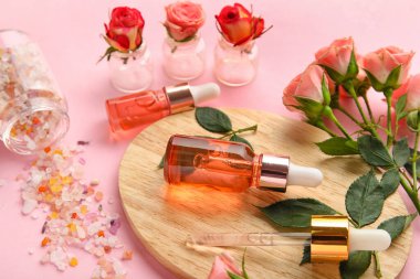 Kütikül yağı şişeleri, deniz tuzu ve pembe arka planda güzel gül çiçekleri, yakın plan.