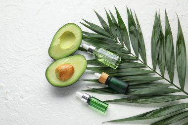 Hafif arka planda tırnak eti yağı, avokado ve palmiye yaprağı şişeleri ile kompozisyon