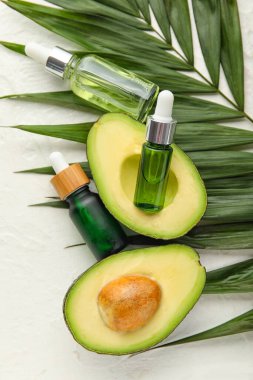 Hafif arka planda tırnak eti yağı şişeleri, avokado ve palmiye yaprağı bileşimi, yakın plan