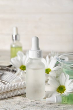 Bir şişe manikür yağı ve papatya çiçekleri açık ahşap masada, yakın plan.