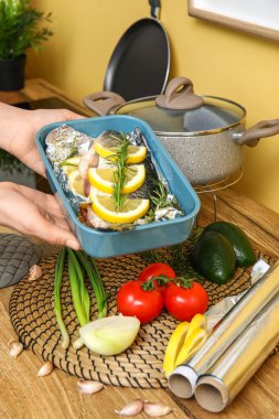 Mutfakta çiğ balık ve sebzeli fırın tabağı tutan bir kadın.