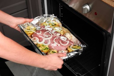 Kadın fırına çiğ et ve sebze ile fırın koyuyor, yakın plan.