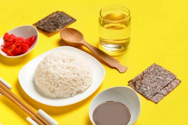 Sarı arka planda lezzetli suşi ruloları hazırlamak için malzemeler içeren kompozisyon