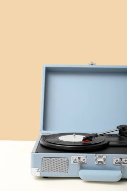Bej duvarın yanındaki masada vinil diski olan kayıt çalar
