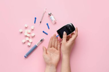 Pembe arka planda glukometre kullanan bir kadın. Diyabet kavramı