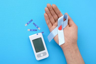 Mavi arka planda farkındalık kurdelesi ve glukometresi olan bir kadın. Diyabet kavramı