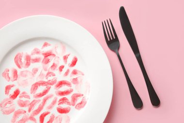 Pembe arka planda ruj izi ve çatal bıçak takımı olan bir tabak.