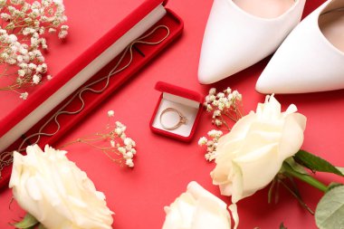 Kırmızı arka planda nişan yüzüğü, kolye, topuklu ve çiçekli kutular.