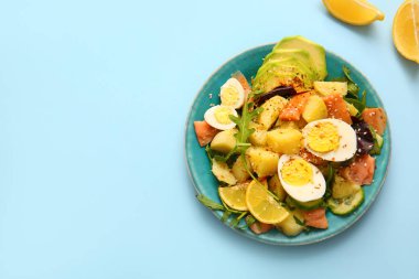 Açık mavi arka planda yumurta ve avokado ile lezzetli patates salatası tabağı.