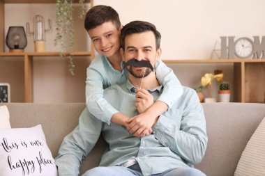 Evde kağıt bıyıklı babasının ve küçük oğlunun portresi.