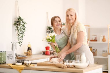 Genç bir kadın mutfakta lalelerle annesini selamlıyor.